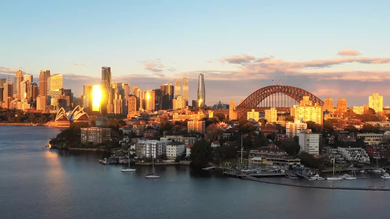 Sydney Harbour at sunset, with the Opera House and Harbour Bridge lit by the setting sun and a marina in the foreground.